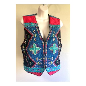 May include: A sleeveless vest featuring a combination of black and blue denim panels. The garment is decorated with vibrant, multi-colored embroidery in floral and geometric patterns, including bright red shoulder sections and a front zipper closure.