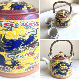 May include: A yellow ceramic teapot and two cups with a dragon design. The teapot has a woven handle and a lid with a dragon motif. The cups and teapot feature blue dragons, red accents, and a yellow background.