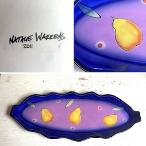 May include: An elongated, scalloped-edge glass tray featuring a gradient purple center and deep blue border. The surface is decorated with three yellow pears, green leaves, and small red dots. The signature Natali Warrens 2011 is visible.