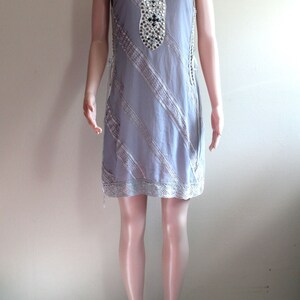 May include: A sleeveless grey dress with a white lace trim and a beaded neckline. The dress is on a mannequin.