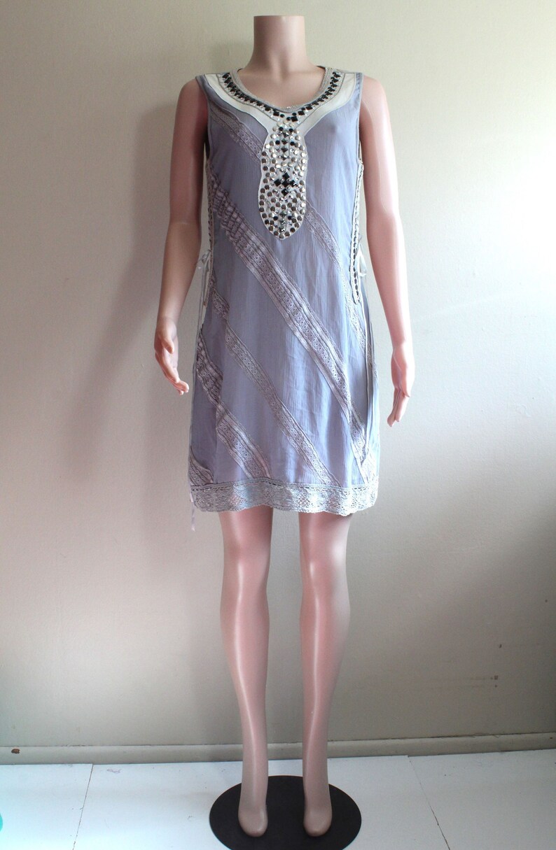May include: A sleeveless grey dress with a white lace trim and a beaded neckline. The dress is on a mannequin.