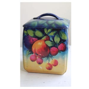 May include: A vintage square tin box with a blue lid and a handle. The box is decorated with a colorful illustration of fruit, including apples, pears, and strawberries.