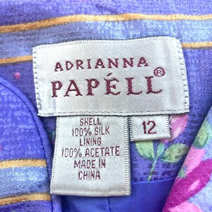 May include: Close-up of a label from an Adrianna Papell garment. The label is white with the brand name in burgundy. The label indicates the shell is 100% silk, the lining is 100% acetate, and it is made in China. The size is 12.