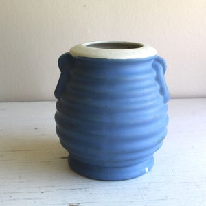 May include: A blue ceramic vase with a white rim and two handles. The vase has a ribbed design.