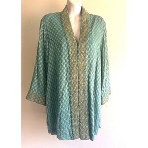 May include: A teal open-front jacket featuring a repeating gold-toned floral pattern across the fabric. The garment includes long sleeves and a wide, vertical band of intricate gold embroidery running along the front opening and sleeve cuffs.