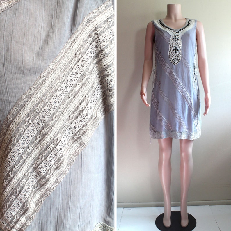 May include: A sleeveless, light grey dress with a white lace trim and a beaded design on the front. The dress is made of a soft, flowing fabric.
