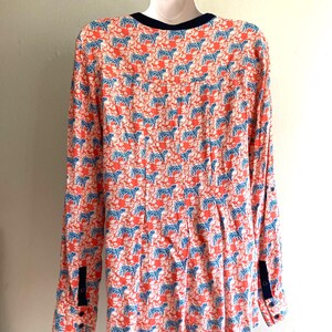 May include: A long-sleeved blouse with a vibrant pattern of blue zebras on a coral background. The blouse features a navy blue trim on the collar and cuffs, and is hanging on a white hanger.