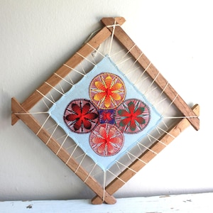 May include: A wooden frame with four colorful embroidered circles in the center. The circles are red, orange, yellow, and green. The frame is made of natural wood and has a light blue background.