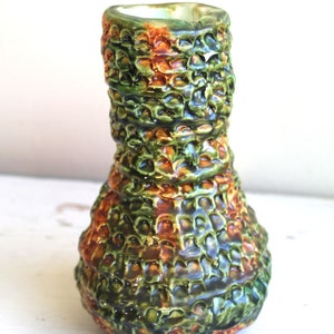 Könnte beinhalten: Eine grüne und orangefarbene Keramikvase mit strukturierter Oberfläche. Die Vase hat einen breiten Boden und einen schmalen Hals.