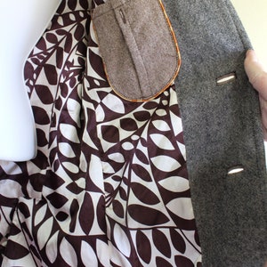 May include: A grey tweed blazer with a brown leaf patterned lining and a brown tweed pocket. The blazer has three buttons on the front.