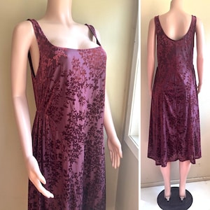 May include: A sleeveless midi dress in a deep plum shade featuring a dark floral velvet burnout pattern. The garment has a wide scoop neckline, thick shoulder straps, and a relaxed, flowing silhouette that falls below the knee in length.