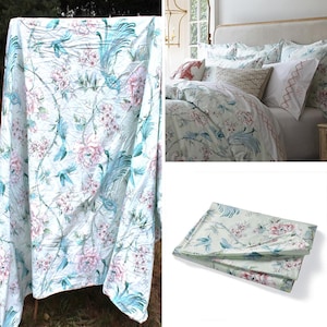 May include: A white duvet cover with a floral pattern featuring blue birds and pink flowers. The duvet cover is shown folded and laid flat on a white surface.