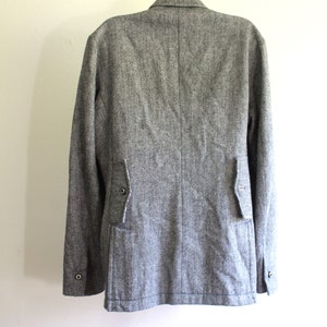 May include: A grey tweed blazer with a single button fastening and two flap pockets on the back.