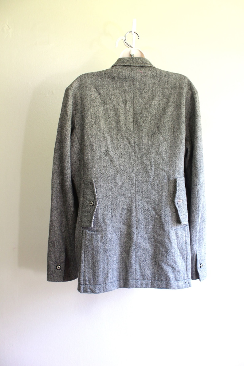 May include: A grey tweed blazer with a single button fastening and two flap pockets on the back.