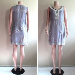 May include: A sleeveless, light blue dress with a white lace trim and a beaded design on the front. The dress has a straight silhouette and a relaxed fit.
