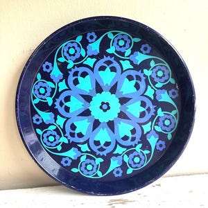 May include: A round metal serving tray featuring a dark navy blue background with a vibrant central mandala pattern in shades of light blue and turquoise. The design includes stylized floral motifs and symmetrical geometric shapes.