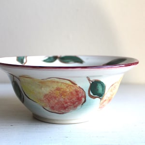 Puede incluir: Cuenco de cerámica blanca con diseño de pera pintado a mano. El cuenco presenta peras amarillas, rojas y verdes con hojas verdes. El borde está adornado con una fina línea roja. Un artículo de cocina decorativo.