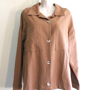 May include: A white ceramic mug with a black handle and the text "But First, Coffee" in a bold, black font. The mug is set against a blurred background, suggesting a cozy setting.