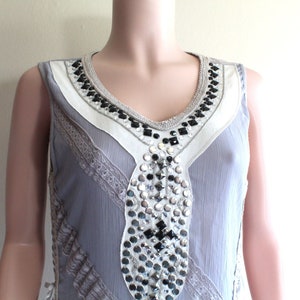 May include: A sleeveless grey dress with a white and black beaded neckline and silver and black embellishments.