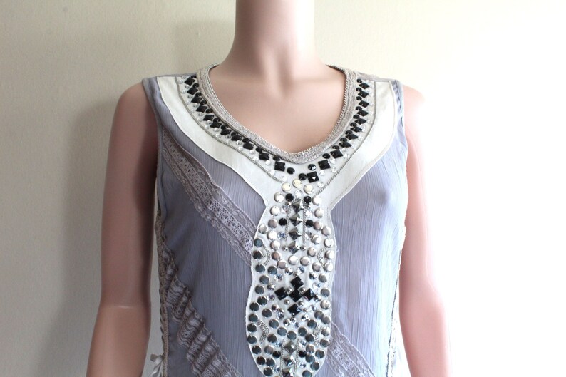 May include: A sleeveless grey dress with a white and black beaded neckline and silver and black embellishments.