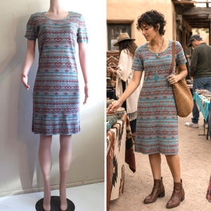 May include: A short-sleeved knee-length dress in a light blue hue featuring a repeating horizontal pattern of geometric shapes in shades of red and dark blue. The garment has a round neckline and a straight-cut silhouette that falls to the knees.