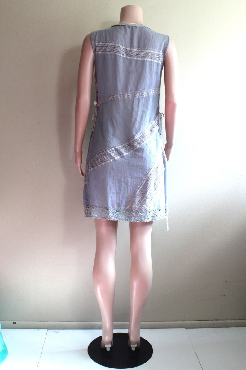 May include: A light blue sleeveless dress with a white and light brown patterned design. The dress has a lace trim at the hem and is cinched at the waist.