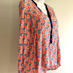May include: A long-sleeved blouse with a vibrant pattern of blue animal figures on a coral background. The blouse features a V-neckline with navy trim and a button-down front. The fabric appears lightweight and suitable for warmer weather.