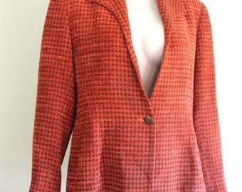 Könnte beinhalten: Ein orangefarbener Blazer mit einem kleinen, sich wiederholenden Muster. Der Blazer hat einen einzelnen Knopfverschluss und ein klassisches Revers. Der Stoff scheint ein strukturiertes Gewebe zu sein. Der Blazer wird auf einer Schaufenquin präsentiert.