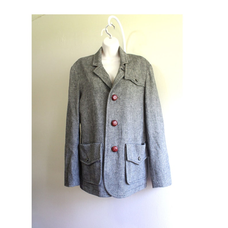 May include: A grey tweed blazer with four large red buttons and two large pockets. The blazer has a classic collar and a relaxed fit.