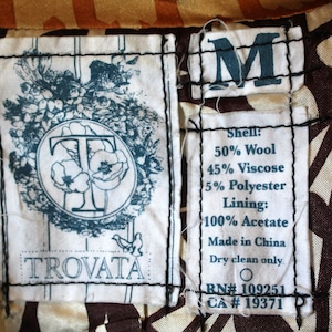 May include: A white tag with black stitching and the text "TROVATA" in black lettering. A blue tag with the letter "M" in white lettering. A white tag with black stitching and the text "Shell: 50% Wool 45% Viscose 5% Polyester Lining: 100% Acetate Made in China Dry clean only RN# 109251 CA # 19371".