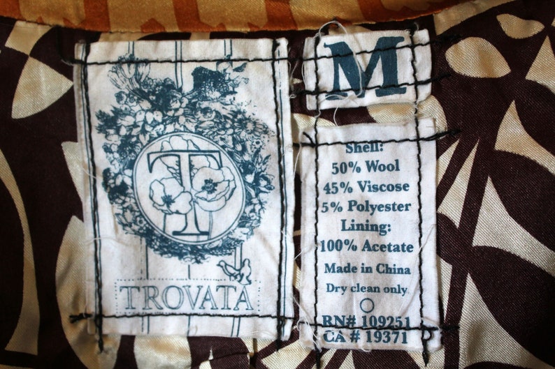May include: A white tag with black stitching and the text "TROVATA" in black lettering. A blue tag with the letter "M" in white lettering. A white tag with black stitching and the text "Shell: 50% Wool 45% Viscose 5% Polyester Lining: 100% Acetate Made in China Dry clean only RN# 109251 CA # 19371".
