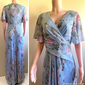 Op de afbeelding: Een lichtblauwe, vloerlange jurk met een bloemenpatroon van roze en groene bloemen. De jurk heeft een V-hals, korte fladdermouwen en een geplooide textuur. De jurk wordt op een mannequin getoond.