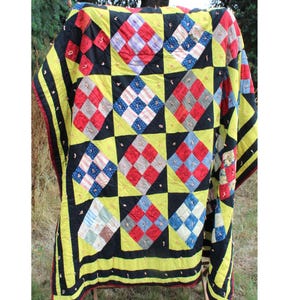 May include: A vintage quilt with a patchwork design featuring squares of red, blue, yellow, and white fabric. The quilt is made up of a grid of squares, with each square containing a different pattern. The quilt is edged with a yellow border.