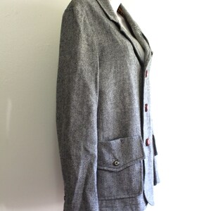 May include: A grey tweed blazer with a single button closure and a patch pocket on the left side. The blazer has a brown button and a brown lining.