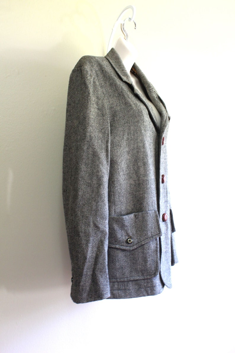 May include: A grey tweed blazer with a single button closure and a patch pocket on the left side. The blazer has a brown button and a brown lining.