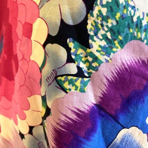 May include: A fabric featuring a vibrant floral pattern on a black background. The design includes large, stylized flowers in shades of bright pink, deep purple, and blue, accented by light blue blossoms and green, yellow, and white textured leaves.