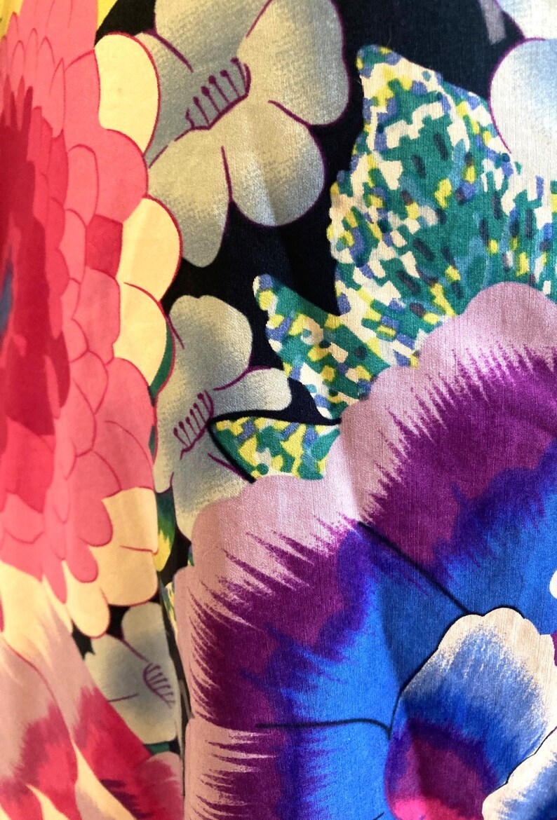 May include: A fabric featuring a vibrant floral pattern on a black background. The design includes large, stylized flowers in shades of bright pink, deep purple, and blue, accented by light blue blossoms and green, yellow, and white textured leaves.