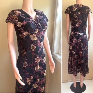 May include: A black midi dress featuring short sleeves, a V-neckline, and a velvet floral pattern in shades of burgundy and beige. The garment displays a fitted bodice and a flowing skirt, shown from both the front and back views on a mannequin.