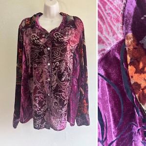 May include: A long-sleeve button-down shirt in deep shades of purple, magenta, and orange. The fabric features a textured velvet finish with an intricate floral and paisley pattern throughout. The shirt includes a classic collar and white buttons.