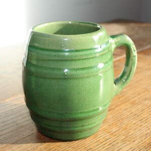 May include: A green ceramic mug shaped like a barrel with a handle. The mug has a crackled glaze and is a vintage style.