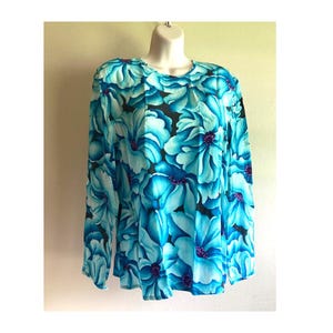 May include: A long-sleeved blouse featuring a vibrant floral pattern in shades of turquoise, cyan, and deep blue against a black background. The garment has a round neckline and a relaxed fit, showcasing large, layered flower petals throughout.