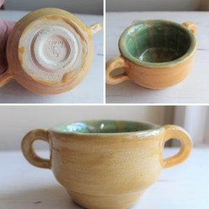 Pode incluir: Uma tigela de cerâmica amarela com duas alças e um esmalte verde no interior. A tigela tem uma forma ligeiramente arredondada e um acabamento liso e brilhante.