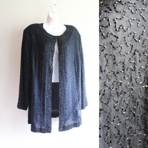 Peut inclure: Un cardigan noir en perles avec un long devant ouvert et des manches longues. Le cardigan est fait d'un tissu fin et délicat et est orné de petites perles argentées.