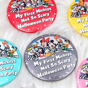 Peut inclure: Une collection de badges ronds avec des illustrations de personnages de dessins animés en costumes de squelette. Le texte My First Mickeys Not So Scary Halloween Party est imprimé sur chaque badge en lettres blanches sur fond coloré.