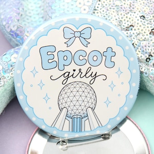 May include: A circular pin-back button featuring a light blue scalloped border, a small blue bow, and the text Epcot girly in blue script. Below the text is a graphic illustration of the Spaceship Earth structure in black and white lines.
