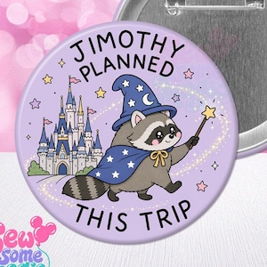 Op de afbeelding: Een ronde button met een lichtpaarse achtergrond met een cartoon wasbeer die een blauwe tovenaarshoed en cape draagt en een sterrenstaf vasthoudt. Op de achtergrond staat een kasteel met de tekst JIMOTHY PLANNED THIS TRIP in zwarte letters.