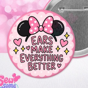 May include: A round pinback button featuring a pink scalloped background with black mouse ears and a pink polka-dot bow. The text reads EARS MAKE EVERYTHING BETTER in black letters, surrounded by small pink hearts and yellow four-pointed stars.