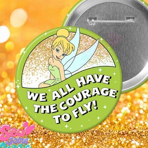 May include: A round pinback button featuring a cartoon fairy with blonde hair and light blue wings against a gold glitter background. The lower portion is lime green with the black text, WE ALL HAVE THE COURAGE TO FLY! The back is silver metal.