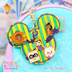 May include: A Mickey Mouse-shaped pin holder with a gold clasp, featuring various character pins. The holder has a green and yellow striped background with purple accents and a decorative border. The pins include a pumpkin carriage, Scar, and other characters.