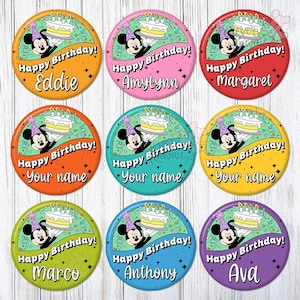Puede incluir: Nueve botones redondos y coloridos con un diseño de dibujos animados de Mickey Mouse sosteniendo un pastel de cumpleaños. Cada botón tiene el texto "Happy Birthday!" y un nombre o "Your name". Los botones son de varios colores.